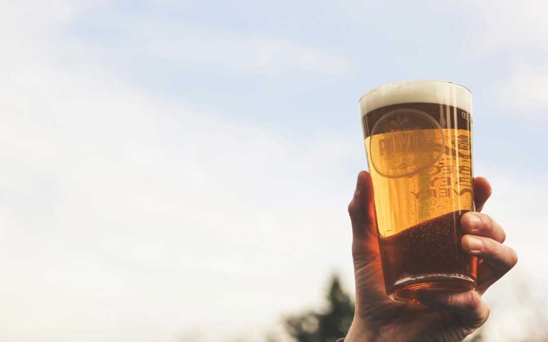 A hand holding a pint of craft beer against the sky, illustrating a casual outdoor setting.