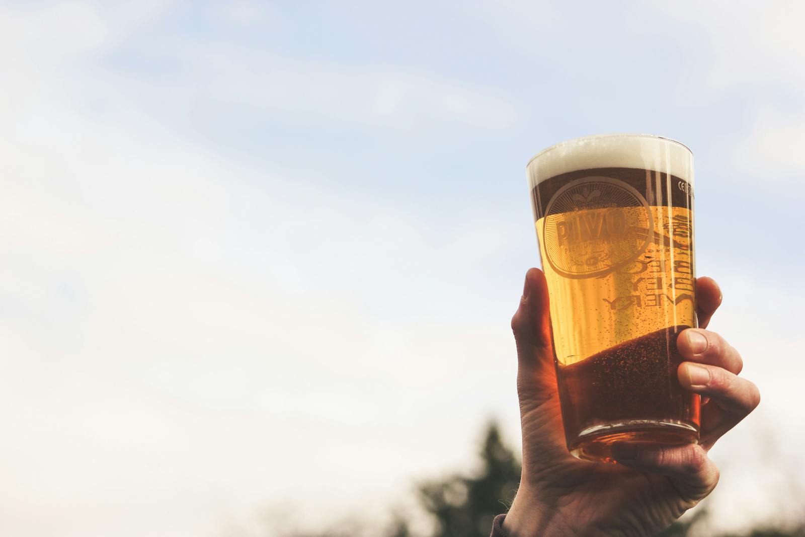 Photo by Jess Low A hand holding a pint of craft beer against the sky, illustrating a casual outdoor setting.