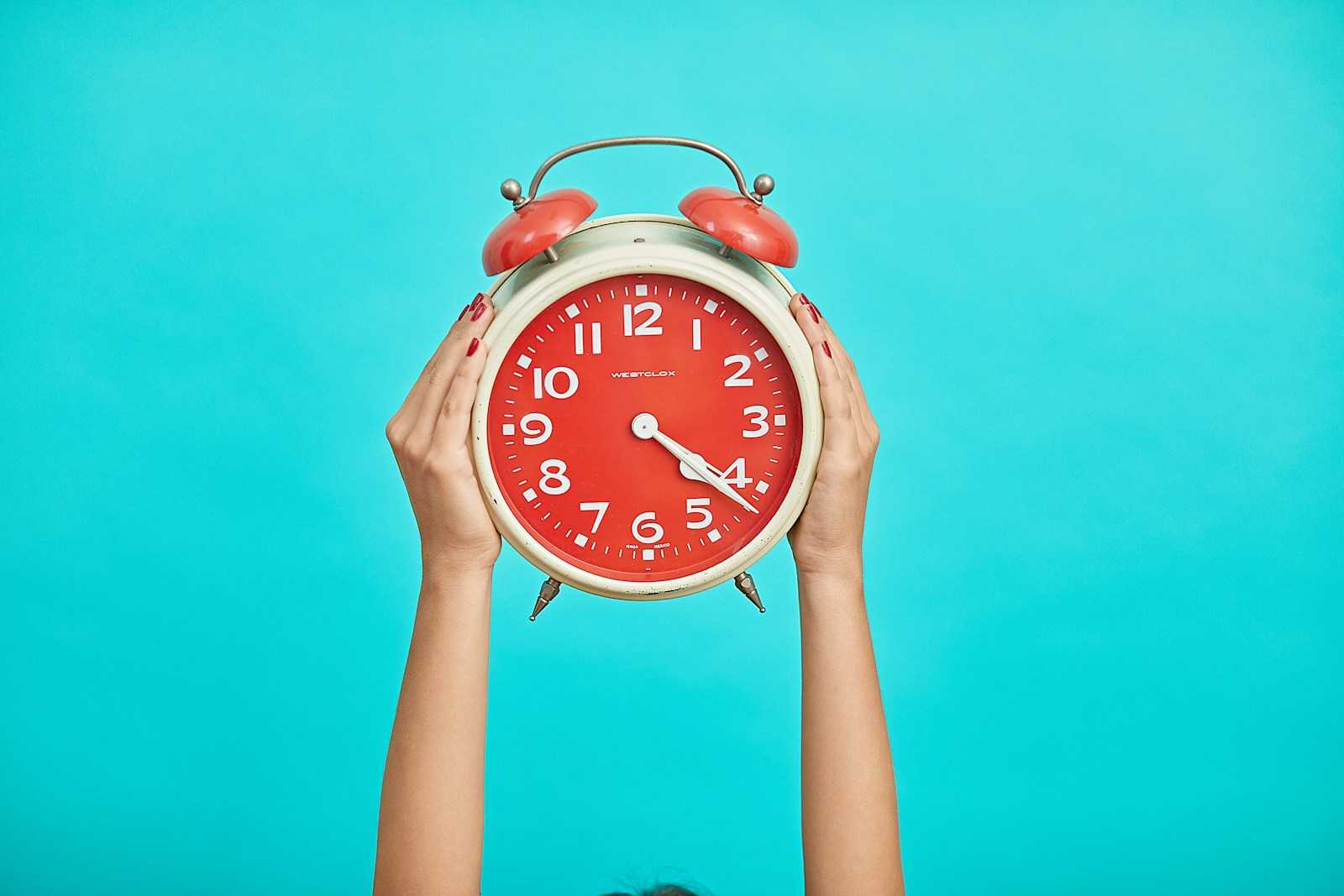 Photo by Malvestida person holding red and beige twin bell analog alarm clock